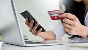 A woman holding a credit card in front of a laptop.